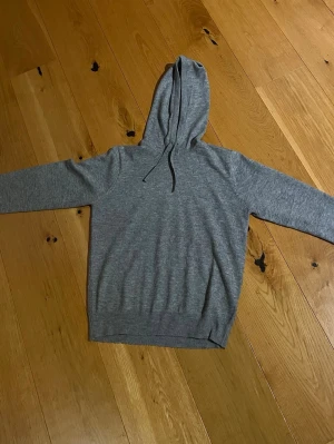 Grå hoodie med dragsko - En enkel och stilren grå hoodie med huva och dragsko. Tillverkad i mjukt material som känns skönt mot huden. Perfekt för dig som gillar en clean och avslappnad look. Passar till det mesta och är lätt att matcha med andra plagg. 