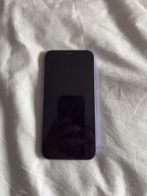 Lila iPhone 12 med dubbla kameror - Säljer en lila iPhone 12 med sprucken baksida, funkar jättebra. Tillverkad i glas och metall, modern design och stilren look. Funkar jättebra bara baksidan men det täcks när man har skal på☺️