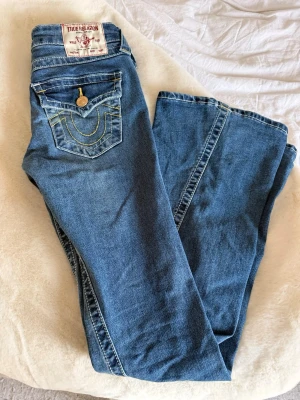 Blå True Religion jeans - Säljer ett par blå jeans från True Religion med guldknappar på bakfickorna i storlek W23. Jeansen är endast använda några fåtals gånger, men passar inte längre därav säljs. 🥰