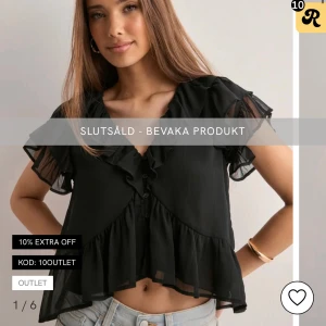 Svart blus med volanger och knappar - Snygg svart blus med volanger längs v-ringningen och nederkanten. Blusen har korta, transparenta ärmar och knappar framtill. Den är croppad och har en luftig passform. Den är i storlek 36 och är aldrig använd.