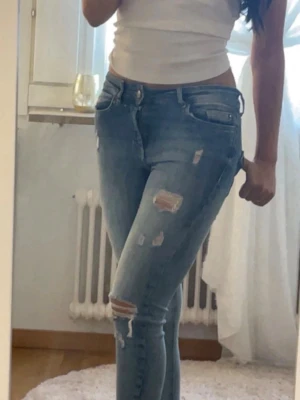 Ljusblå slitna skinny jeans - Säljer ett par ljusblå skinny jeans med slitningar och hål på låret och knät. Jeansen har klassisk femficksmodell och hög midja. Perfekta för en avslappnad och trendig look.