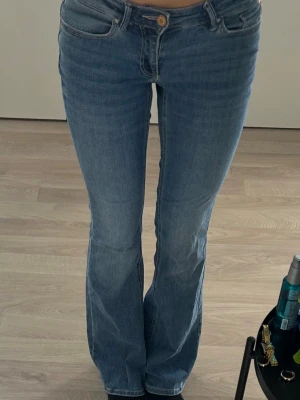 Blå bootcut jeans med låg midja - Säljer ett par klassiska blå bootcut jeans med låg midja och fem fickor. Jeansen har en snygg tvätt och stängs med knapp och dragkedja. Perfekta för dig som gillar en avslappnad men trendig look.