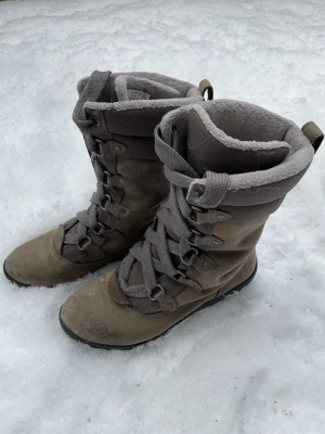 Timberland Grå fodrade vinterkängor med snörning - Säljer ett par grå vinterkängor med högt skaft och snörning framtill. Kängorna har mjukt och varmt foder på insidan och är perfekta för kalla dagar. Yttermaterialet är slitstarkt tyg och syntet. Snygg och praktisk design för vintern.