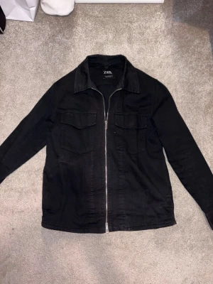 Svart overshirt från Zara - Stilren svart overshirt från Zara i stl S. Materialet är kraftigt bomullstyg som ger en avslappnad men snygg look. Perfekt att bära över en t-shirt/tunn tröja för en trendig lager-på-lager stil. Hör av dig vid frågor och du deringar!
