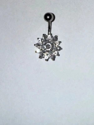 Glittrande navelpiercing med blomma - Säljer en snygg navelpiercing i silverfärg med en stor, glittrande blomma av klara stenar. Blomman har flera kronblad och ger ett riktigt lyxigt intryck. Perfekt för dig som vill ha något som sticker ut och glänser.