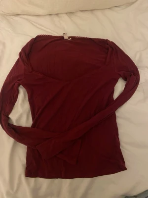 Vinröd långärmad topp från Nelly - Vinröd långärmad topp från Nelly med v-ringad hals och spetsdetalj längs urringningen. Tunn och mjuk i materialet, perfekt att styla med jeans eller kjol. Enkel men ändå snygg design som passar till många olika looks.