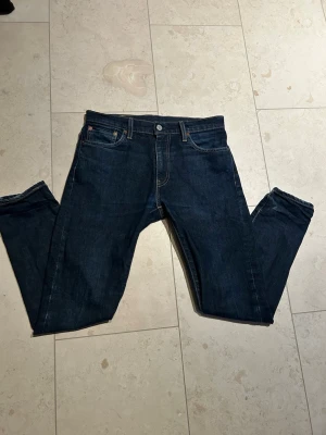 Marinblå Levis 512 - Ett par riktigt fets Levis 512! Dessa är i mycket fint skick och har några små slitningar som gör de ännu snyggare. Köpta på NK. Hör av er vid intresse!