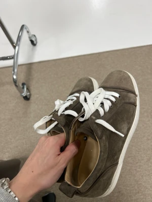 Christian Louboutin sneakers  - Snygga sneakers i brun mocka med vita snören och vit sula. Klassisk låg modell som passar till det mesta. Skorna har en enkel och stilren design utan synliga loggor eller märken. Perfekta för dig som gillar en clean look. Givetvis är skorna äkta och en tvätt görs före dom fraktas! Storleken är 41 men passar 42