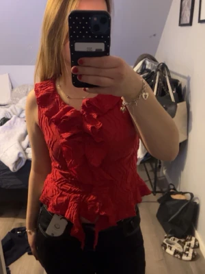 Röd volang topp med knyt - Snygg röd topp med volangdetaljer framtill och längs nederkanten. Toppen är ärmlös och har ett knyt i midjan för extra passform. Perfekt för dig som vill sticka ut med färg och detaljer. Storlek 158/164 men passar mig som har S