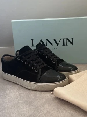 Lanvin skor - Snygga svarta sneakers från Lanvin med lackad tå och ovandel i mocka. Skorna har svarta snören, vit sula och klassisk låg profil. Perfekta för dig som gillar stilrena och exklusiva sneakers med en twist.