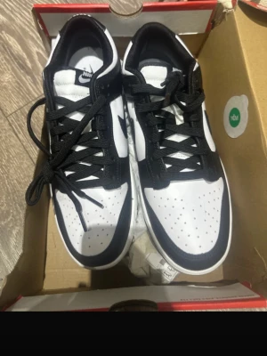 Nike svartvita Dunk Low sneakers panda - Aldrig använda!!                                                   Snygga svartvita Nike Dunk Low sneakers med klassisk siluett. Skorna har svart sula, vita partier med svarta detaljer och svarta skosnören. Ovandelen är i läder med perforerad tåbox för extra ventilation. Perfekta för dig som gillar streetwear och stilrena färger. 