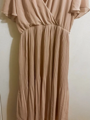 Rosa sommar klänning  - Säljer en rosa långklänning med omlottliv och plisserad kjol. Klänningen har korta volangärmar och ett luftigt, elegant fall. Perfekt för dig som gillar en feminin och stilren look.