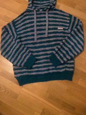 Marni - Mysig hoodie med huva i blått och grått randigt mönster. Tröjan har breda muddar vid ärmslut och nederkant samt dragsko i huvan. Materialet är fluffigt och ger en avslappnad vibe. Liten patchdetalj på bröstet Orginal pris 10000 mitt pris 3500 använd 4 gånger skriv om ni har frågor eller diskutera pris