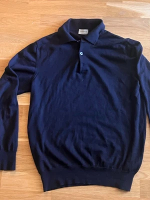 Mörkblå stickad tröja från Morgano - Snygg mörkblå stickad tröja från Morgano med klassisk krage och knappslå framtill. Köpt på Lund och Lund, Nybrogatan. Tillverkad i Italien och har långa ärmar samt ribbade muddar vid ärmslut och nederkant. 