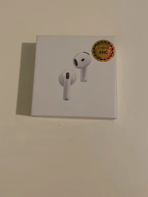 Airpods 4 - Säljer ett par vita trådlösa hörlurar. Snygg och stilren design med laddningsetui. Perfekta för musik, poddar och samtal. Kommer i originalförpackning med tydlig illustration på framsidan.