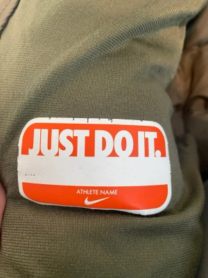 Nike hoodie i olivgrönt XL - Säljer en olivgrön hoodie från Nike med klassisk logga och 'Just Do It.'-märke. Hoodien har en sportig design och är tillverkad i mjukt material som är skönt att bära. Perfekt för dig som gillar streetwear och vill ha något trendigt och bekvämt.