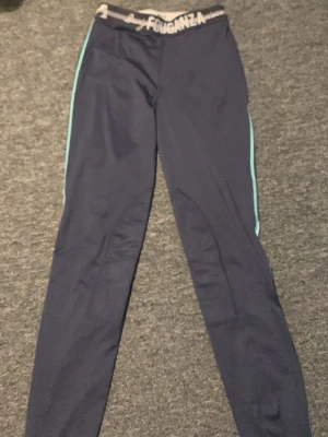 Mörkblå ridbyxor från Fouganza  - Snygga mörkblå leggings från Fouganza med ljusblå detaljer längs sidorna och elastisk midja med logotyp. Perfekta för dig som gillar att rida och vill ha bekväma byxor med bra passform.