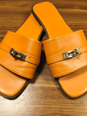 Brown Giulia Sandals  - Stylish brown Giulia sandals in faux leather with a wide strap and unique metal buckle at the front. The sandals have a square toe and flat sole, which gives a modern vibe. Perfect for those who like minimalist design with a twist. Fits size 38-40