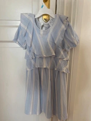 Blåvit randig volangklänning - Söt kortklänning med blå och vita ränder, volangdetaljer över bröstet och puffiga korta ärmar. Klänningen har en luftig passform och rund halsringning. Perfekt för varma dagar och ger en fräsch sommarkänsla.