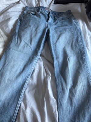Ljusblå raka jeans med rå kant - Säljer ett par ljusblå jeans med rak passform och rå, fransig kant längst ner på benen. Klassisk femficksmodell i mjuk denim. Perfekta för en avslappnad och trendig look. (Andvända 1 gång då jag inte tycker jag passar i baggy jeans)