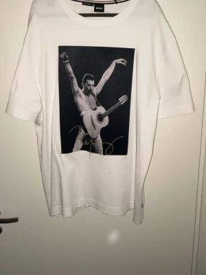 Vit BOSS t-shirt med print - Vit t-shirt från BOSS med stort svartvitt print av en gitarrspelande person på framsidan och citatet 'I'm not going to be a star. I'm going to be a legend!' på ryggen. Klassisk rund hals och korta ärmar. Perfekt för dig som gillar statement-plagg.