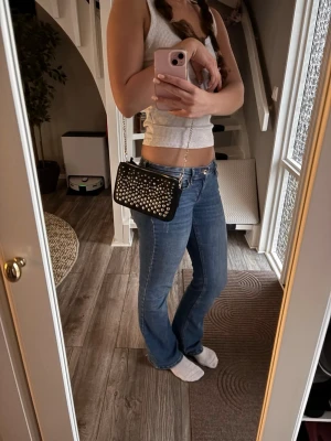 Svart axelväska med nitar - Cool svart axelväska med silvriga nitar och kedjerem. Väskan har dragkedja upptill och är perfekt för att bära det viktigaste. Materialet ser ut som konstläder och designen är både edgy och stilren.