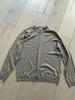 Beige stickad tröja från NN07 - Snygg beige stickad tröja från NN07 med rund halsringning och långa ärmar. Tillverkad i tunt, mjukt material som passar perfekt för lager på lager. Klassisk och stilren design med ribbade muddar vid ärmslut och nederkant. Hör av er vid frågor, priset går att diskutera.