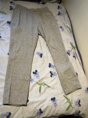 Gråa mjukisbyxor från Nike - Säljer ett par klassiska gråa mjukisbyxor från Nike med enkel design och resår i midjan. Perfekta för chill dagar hemma eller när du vill ha det bekvämt. Tillverkade i mjukt material för extra komfort.