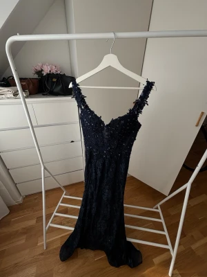 Bal klänning Marinblå Spets  - Jag är 165 det är släp så lång Elegant marinblå långklänning med spetsdetaljer och smala axelband. Klänningen har v-ringning och är dekorerad med blommiga applikationer samt paljetter för extra glans. Perfekt för bal eller festliga tillfällen. 