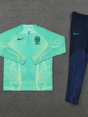 Nike Brasil träningsoverall mint/blå - Snygg träningsoverall från Nike med Brasil-logga. Överdelen är mintgrön med grafiskt mönster, halv dragkedja och lång ärm. Byxorna är mörkblå med mintgrönt Nike-märke och Brasil-tryck, samt diskret mönster. Perfekt för fotbollsträning eller chill.