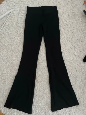 Svarta utsvängda leggings - Säljer ett par svarta yogabyxor med utsvängda ben. De har låg midja och är tillverkade i ett stretchigt material som sitter bekvämt. Perfekta för en trendig och avslappnad stil.