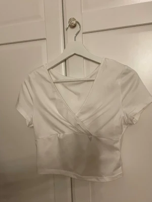 Vit omlottopp med kort ärm - Snygg vit omlottopp med korta ärmar och djup v-ringning. Modellen är croppad och har en stilren, enkel design den SHEIN 