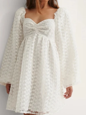 Vit blommig kortklänning med spets NAKD - Söt vit kortklänning med blommigt spetsmönster och långärmade puffärmar. Klänningen har en v-ringad urringning och är tillverkad i ett lätt, luftigt material som passar perfekt till varma dagar. Romantisk och trendig look med fina detaljer, perfekt för studenten. Köpt från NAKD och har endast använts en gång🐚🤍