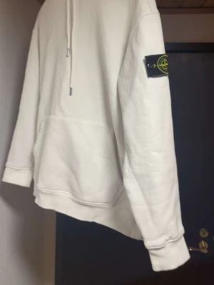 Vit hoodie från Stone Island - Säljer en stilren vit hoodie från Stone Island med klassisk patch på vänster ärm. Hoodien har huva med dragsko och en stor magficka framtill.