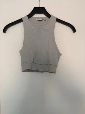 Grå/grön ribbad croppad linnetopp - Snygg grå croppad linnetopp från Lager 157 med ribbad struktur. Toppen är ärmlös och har en tight passform som framhäver axlarna. Perfekt att matcha med höga jeans eller kjol för en trendig look.