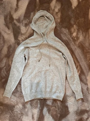 Cashmere hoodie - Mysig ljusgrå hoodie med huva och dragsko. Tillverkad i mjukt material som känns skönt mot huden. Klassisk passform med ribbade muddar vid ärmslut och nederkant. Perfekt för en avslappnad och chill stil.