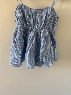 Blåvit randig linnetopp - Säljer en söt blåvit randig linnetopp med smala axelband och rynkad midja. Toppen har en luftig passform och tunna ränder. 