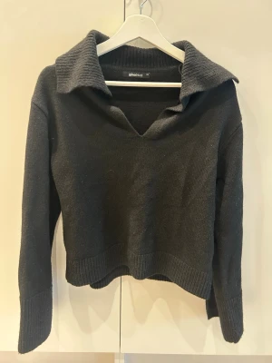 Svart stickad tröja från Gina Tricot - Snygg svart stickad tröja från Gina Tricot med bred krage och v-ringning. Tröjan har långa ärmar med ribbade muddar och en liten slits vid ärmsluten. 