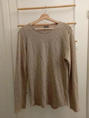 Beige melerad tröja från Åhléns - Långärmad tröja i beige melerad färg från Åhléns. Tröjan har rund halsringning och är gjord i ett mjukt, tunt material som känns skönt mot huden. Enkel och stilren design som är lätt att matcha med olika outfits.