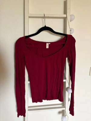 Mörkröd långärmad topp med v-ringning - En mörkröd långärmad topp med v-ringning och slim passform. Perfekt att styla med jeans eller kjol. Materialet känns mjukt och stretchigt, vilket gör den bekväm att bära hela dagen. Enkel och stilren design utan mönster eller extra detaljer. Använd en gång!