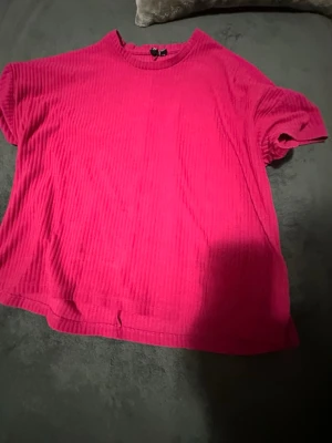 Rosa ribbat set med t-shirt och shorts - Säljer ett mjukt och bekvämt set i starkt rosa färg, består av en ribbad t-shirt med rund hals och korta ärmar samt matchande shorts med bred resår i midjan. Perfekt för chill dagar hemma eller som mysplagg. Materialet känns lent och stretchigt.