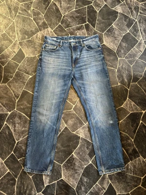 Blå raka jeans Vaillent - Säljer ett par klassiska blå jeans från Vaillent med rak passform och fem fickor. Jeansen har snygga slitningar och kontrastsömmar. Dock finns det några små svarta fläckar vid högerbakficka. Storlek W32 L30