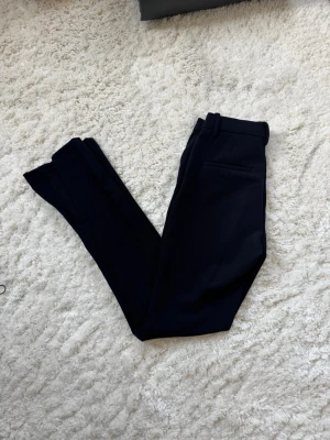 Svarta kostymbyxor med smal passform - Snygga svarta kostymbyxor med smal passform och klassiska detaljer som bälteshällor och bakficka. Perfekta för en clean och stilren look. Materialet känns mjukt och har en lätt stretch för extra komfort.