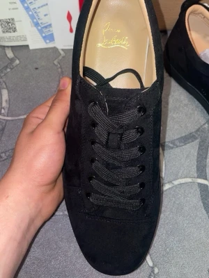 Svarta sneakers från Christian Louboutin - Stilrena svarta sneakers från Christian Louboutin i mocka med klassisk låg siluett. Skorna har svarta skosnören, diskret design och ikonisk röd detalj på insidan. Perfekta för dig som gillar exklusiva och tidlösa sneakers.