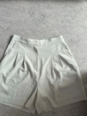 Mint gröna shorts - Stilrena mintgröna shorts som är oanvända. Klassisk design med två fickor bak och bred linning. Perfekta för en fräsch och clean look. Materialet känns mjukt och svalt, troligen bomull eller polyester.