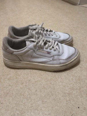 Vita Reebok Club C 85 sneakers - Klassiska vita Reebok Club C 85 sneakers i lågt snitt med ovandel i läder och textildetaljer. Skorna har Reebok-logga på sidan och en bekväm vadderad häl. Perfekta för en clean och tidlös stil.