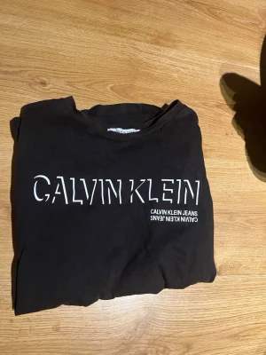 Svart Calvin Klein Jeans t-shirt - Snygg svart t-shirt från Calvin Klein Jeans med stor vit logga framtill. Klassisk passform och rund halsringning. Perfekt för dig som gillar stilrena och trendiga plagg med tydlig branding.
