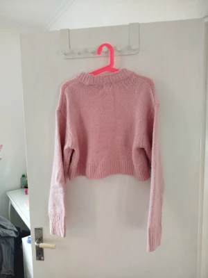 Rosa cropped stickad tröja från H&M - Säljer en rosa cropped stickad tröja från H&M med ribbad halsringning. Tröjan har långa ärmar och är gjord i ett mjukt stickat material.