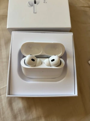 Apple AirPods Pro gen 2 trådlösa hörlurar - Säljer ett par vita Apple AirPods Pro gen 2 med laddningsetui. Hörlurarna är in-ear och har en stilren, kompakt design i blankt plastmaterial. Perfekta för musik, samtal och träning med aktiv brusreducering och touchkontroller.
