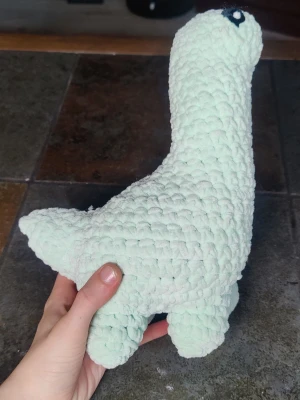 Virkad mintgrön dinosaurie - Söt handvirkad dinosaurie i mjuk, mintgrön plysch. Den har lång hals, fyra ben och svart broderat ögon. Perfekt som dekoration eller gosedjur. Unik och charmig design som sticker ut i rummet.